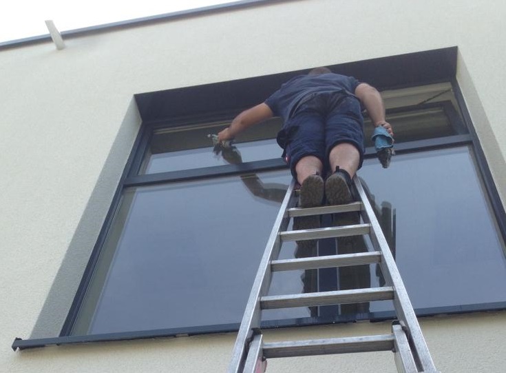 Eine Reinigungskraft bei der Glas- und Rahmenreinigung auf einer Leiter